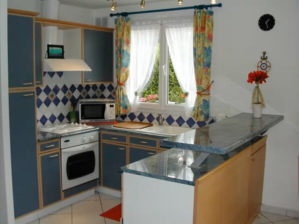 A compact kitchen with a microwave, stove, sink, and a window with curtains.