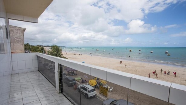 Ein Balkon mit Blick auf einen Strand, einen Parkplatz und ein Schild, das ein Restaurant direkt am Strand kennzeichnet.