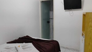 Ein Zimmer mit einem Bett, einer Holztür, einem an der Wand befestigten Fernseher und einer Badezimmertür.