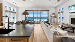 A modern kitchen with a large island, a dining area with a view of the beach, and a cozy seating area with a fireplace. - Gulf-Front Luxury Home w/ Panoramic Views • Private Pool • Carillon Beach (Panama City Beach)
