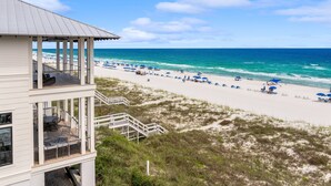 A beach house with a balcony overlooking a sandy beach with umbrellas and people.