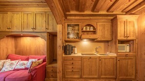 L’intérieur d’un chalet en bois chaleureux comprend un coin cuisine, un canapé rouge agrémenté de coussins à motifs floraux et un plancher en bois.