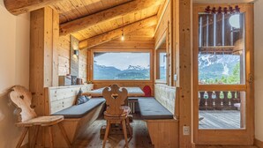 A wooden cabin with a large window offering a mountain view, a bench, and a small table. - Casa Verocip, a panoramic attic with a view of the Dolomites (Cortina d´Ampezzo)