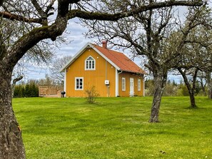 A yellow wooden house with a red roof, surrounded by a green lawn and trees. - 4 Star Holiday Home in Haltorp (Halltorp)