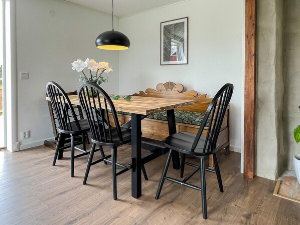 A dining area with a wooden table, black chairs, a bench, a pendant light, and a framed picture on the wall.