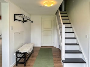A hallway with a bench, a coat rack, a door, and a staircase.
