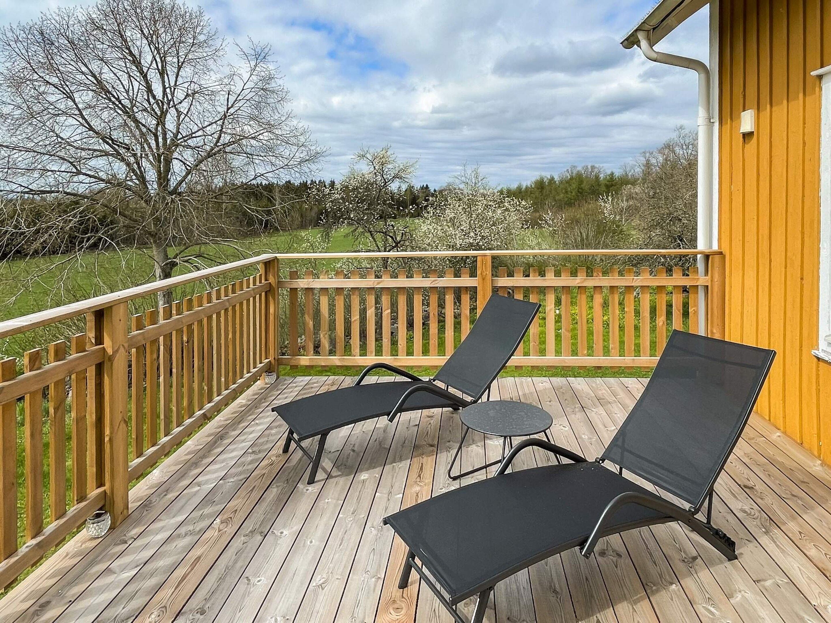 A wooden deck with two black lounge chairs and a small table.