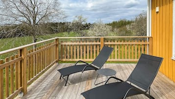 A wooden deck with two black lounge chairs and a small table.