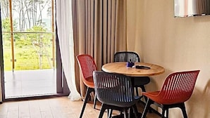 A modern room with a wooden floor, a round table, and four chairs. There is a large window with curtains, a ceiling light, and a wall-mounted TV. - Terrace Kaprovan (Ureki)