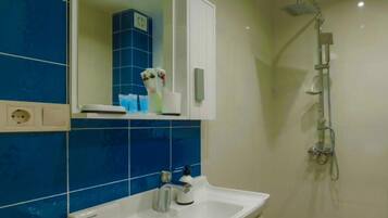 Un baño con lavamanos blanco, azulejos azules, un espejo, ducha y un armario con artículos de aseo.
