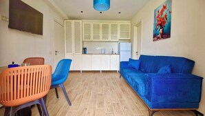 A compact living space with a kitchenette, a blue sofa, and a dining area with orange chairs. - Terrace Kaprovan (Ureki)