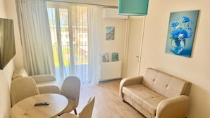 A living room with a beige sofa, two armchairs, a round wooden table, and a painting of flowers on the wall. - Terrace Kaprovan (Ureki)