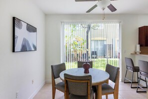 A dining area with a round table, four chairs, a ceiling fan, and a large window with blinds. - Landing | Incredible 3BD, Pool (Homestead)