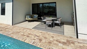 A covered outdoor patio with a pool, a ceiling fan, and a table with chairs.