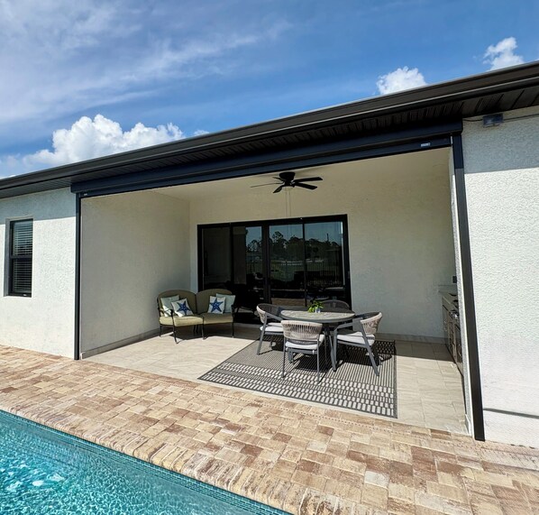 A covered outdoor patio with a pool, a ceiling fan, and a table with chairs.