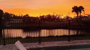 A swimming pool with a chair in the foreground, a fence, and a sunset view in the background.