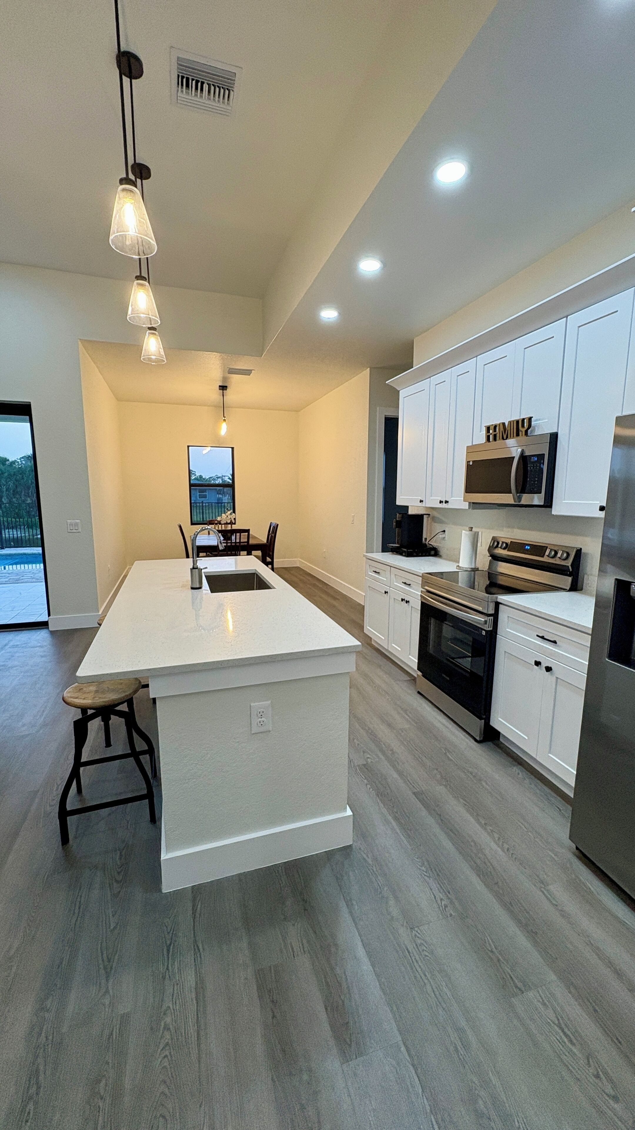 A modern kitchen with a large island, white cabinetry, stainless steel appliances, and pendant lighting.