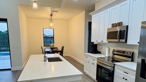 A modern kitchen with a large island, white cabinetry, stainless steel appliances, and pendant lighting.