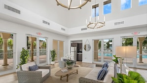 A spacious lobby with wicker furniture, a coffee table, and potted plants. There are glass doors leading to a pool area and an exit sign is visible. - Landing | Stunning 3BD, Pool (Homestead)