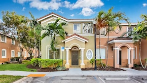 A residential building with a beige facade, a central entrance with a door, and a small porch area. - Landing | Stunning 3BD, Pool (Homestead)