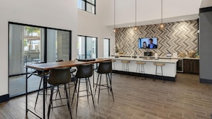 A modern kitchen with a large island, bar stools, and a TV mounted on the wall. - Landing | Incredible 1BD, Pool, Clubhouse (Jacksonville)