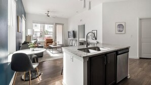 A modern kitchen with a central island, a dining area with a table and chairs, and a living space with a sofa and a TV. - Landing | Incredible 1BD, Pool, Clubhouse (Jacksonville)