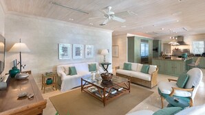 A spacious living room with a sofa, armchairs, a coffee table, and a kitchen in the background.
