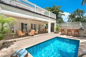 A poolside area with a covered patio, outdoor seating, and a clear blue pool.