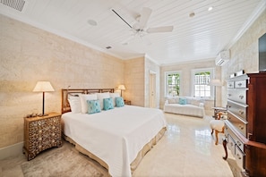 A spacious bedroom with a large bed, a wooden nightstand, a dresser, and a ceiling fan.