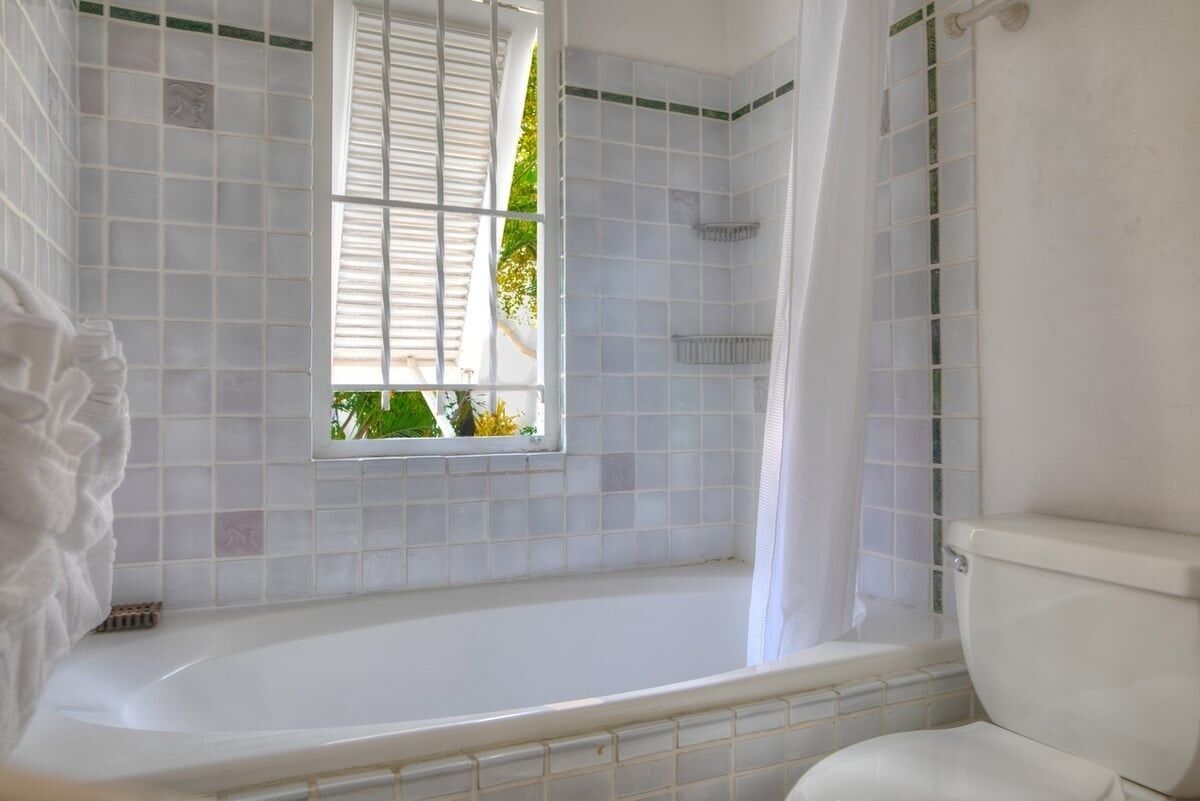 A bathroom with a bathtub, a window, and a toilet.
