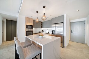 Een moderne keuken met een centraal eiland, roestvrijstalen apparatuur en hanglampen.