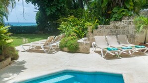 A poolside area with lounge chairs, a clear view of the ocean, and lush greenery. - Waverly House 3 Bedroom Townhouse (Bowling Alley Hill)