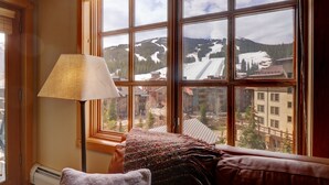 A cozy room with a large window offering a view of a snowy mountain and buildings. - Pp506 Passage Point 1 Bedroom Condo (Copper Mountain)