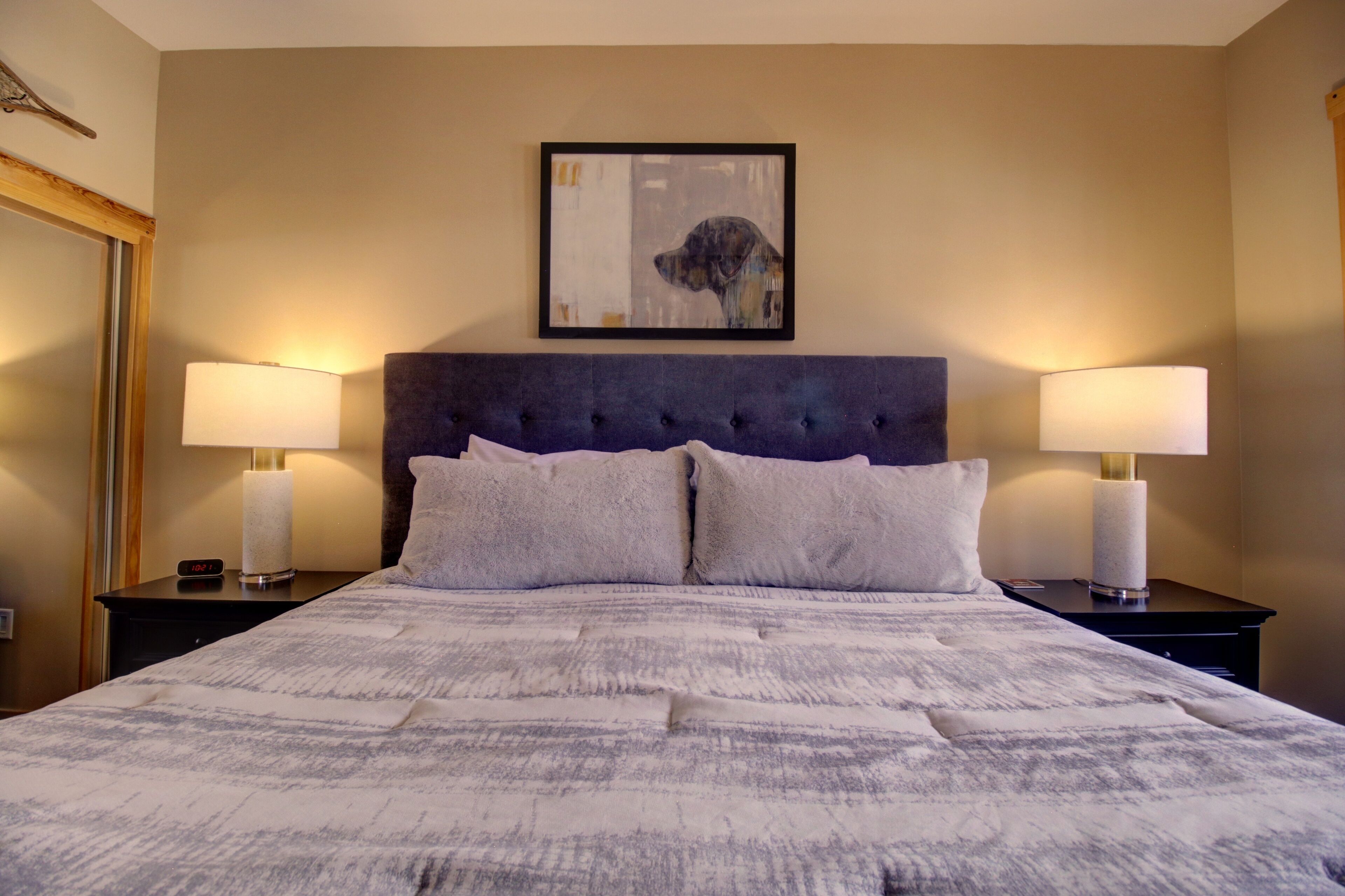 Un lit bien fait, recouvert d’une couvre-lit à motifs, avec deux lampes de chevet et une œuvre d’art encadrée accrochée au mur.