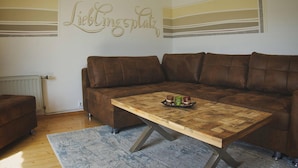 A living room with a brown leather sofa, a wooden coffee table with a tray of candles, and a wall with a decorative sign. - Apartment With Mountain View (Treffen)