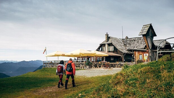 A rustic lodge with a stone facade and a sloped roof, located on a grassy hill with a mountain backdrop. - Apartment With Mountain View (Treffen)