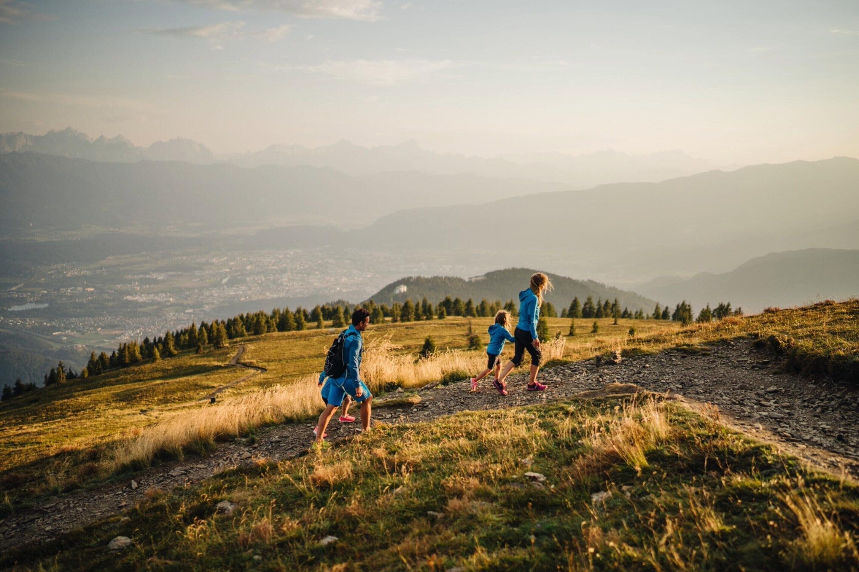 A group of people hiking on a mountain trail with a view of a valley and distant mountains.