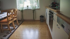 A kitchen with wooden flooring, a dining table with chairs, a window with curtains, a radiator, and a washing machine. - Apartment With Mountain View (Treffen)