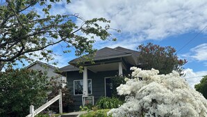 Ein Haus mit einer Veranda, einer Treppe, die zum Eingang führt, und einem großen weißen Busch mit Blüten im Vorgarten.