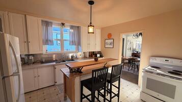 Une cuisine avec des meubles blancs, un îlot central en bois, des chaises noires, une cuisinière blanche et un luminaire suspendu.