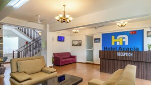 A hotel reception area with a reception desk, sofas, a staircase, and a TV screen. - Hotel Acacia Yelahanka (Bengaluru)
