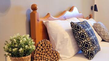 Una cama bien hecha con cabecera de madera, almohadas blancas y estampadas, una cesta tejida con una planta y una pila de leños.