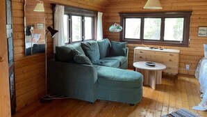 A cozy cabin interior with a green sofa, wooden walls, a small round table, and a window with curtains. - 7 Person Holiday Home in Bjornlunda (Björnlunda)