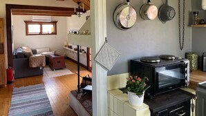A cozy kitchen with a stove, oven, and hanging pots. A living area with a sofa and a window is visible in the background. - 7 Person Holiday Home in Bjornlunda (Björnlunda)