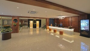 A hotel reception area with a polished marble floor, wooden paneling, and a reception desk with two staff members.