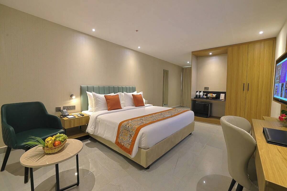 Habitación de hotel con cama, escritorio, silla, una pequeña mesa con fruta y televisor.