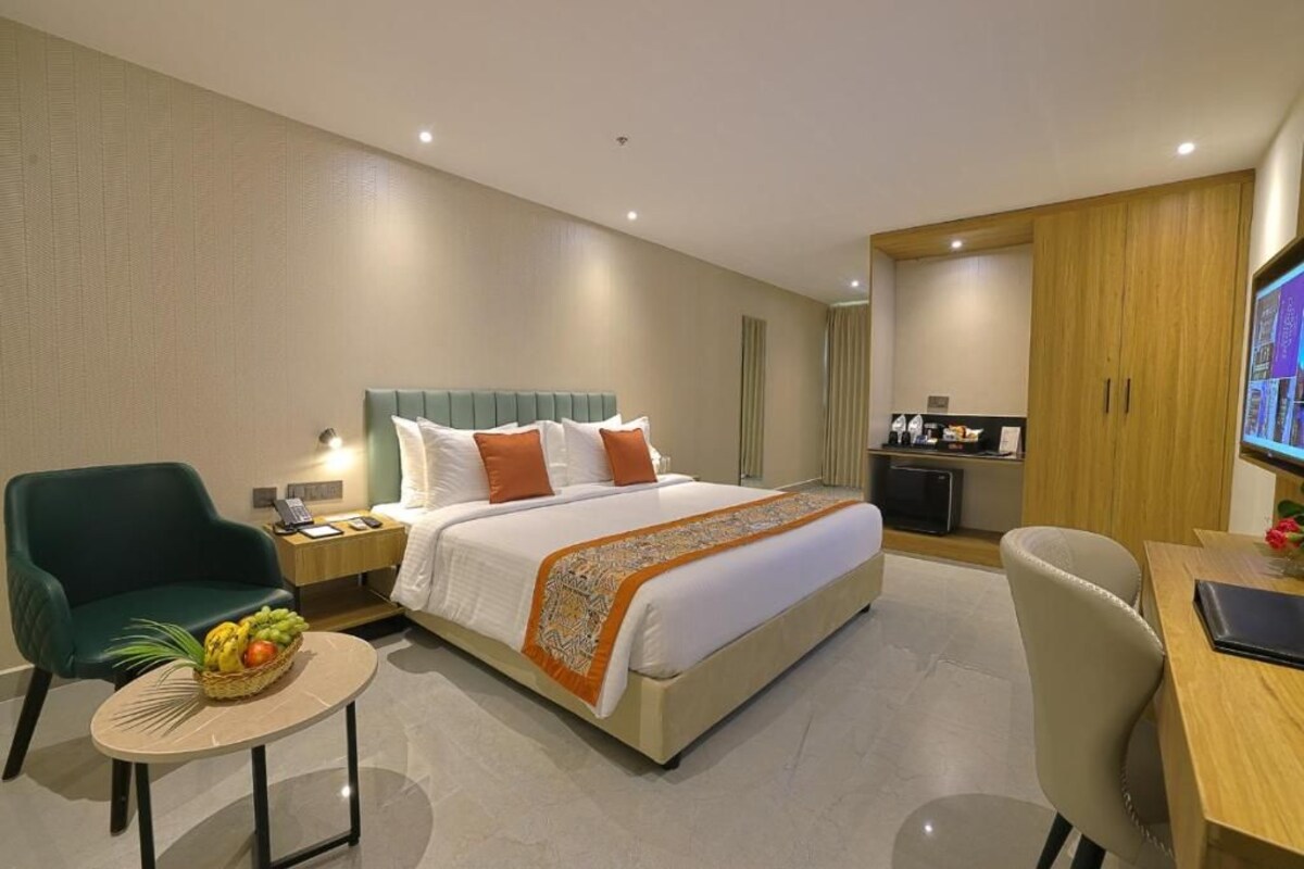 Habitación de hotel con cama, escritorio, silla, una mesita con fruta y televisor.