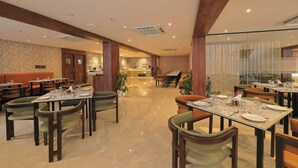 A spacious dining area with multiple tables and chairs, a kitchen in the background, and a modern interior design.
