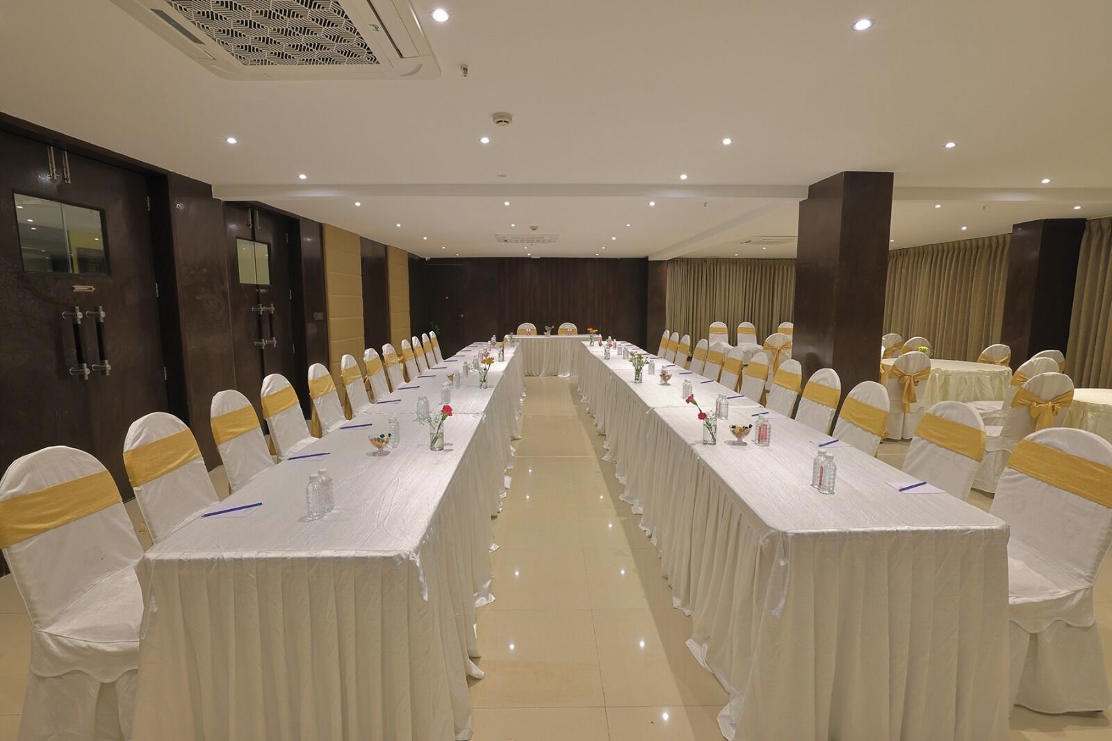 Un salón de conferencias con una larga mesa, sillas adornadas con cintas amarillas y un mantel blanco.