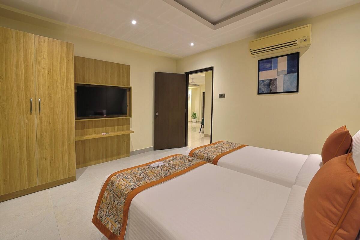 Habitación de hotel con un armario grande, televisión de pantalla plana, cama con ropa de cama estampada y equipo de aire acondicionado.